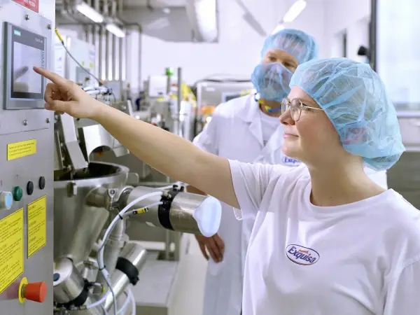 Eine Auszubildende der Produktion steht mit ihrem Ausbilder an einer Produktionsmaschine und lernt deren Bedienung - Nahaufnahme.  Falls nur Kopf: Portrait Marina Hibler, Auszubildende für Lebensmitteltechnik.