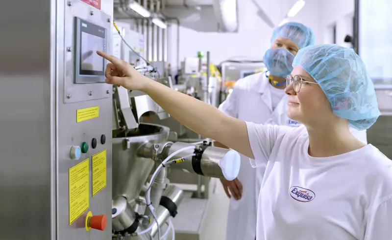 Eine Auszubildende der Produktion steht mit ihrem Ausbilder an einer Produktionsmaschine und lernt deren Bedienung - Nahaufnahme.  Falls nur Kopf: Portrait Marina Hibler, Auszubildende für Lebensmitteltechnik.