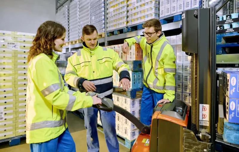 Zwei Auszubildende der Logistik stehen mit ihrem Ausbilder im Kühllager an einer Logistik-Ameise und lernen.