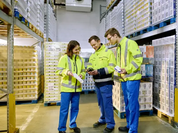 Zwei Auszubildende der Logistik stehen mit ihrem Ausbilder im Kühllager und erhalten eine Erklärung.