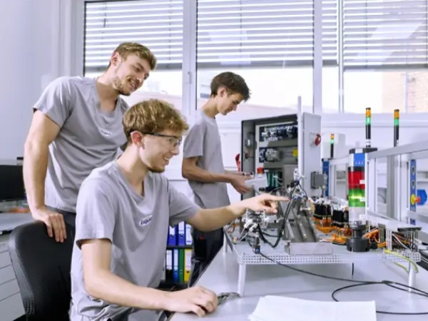 Zwei Mechatroniker-Azubis lernen am Elektropult von ihrem Ausbilder.