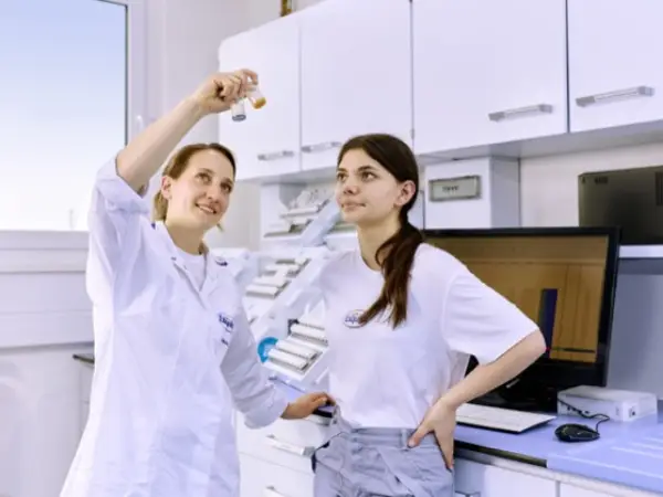 Eine Laborantin-Azubi und ihre Ausbilderin betrachten ein Laborgefäß.