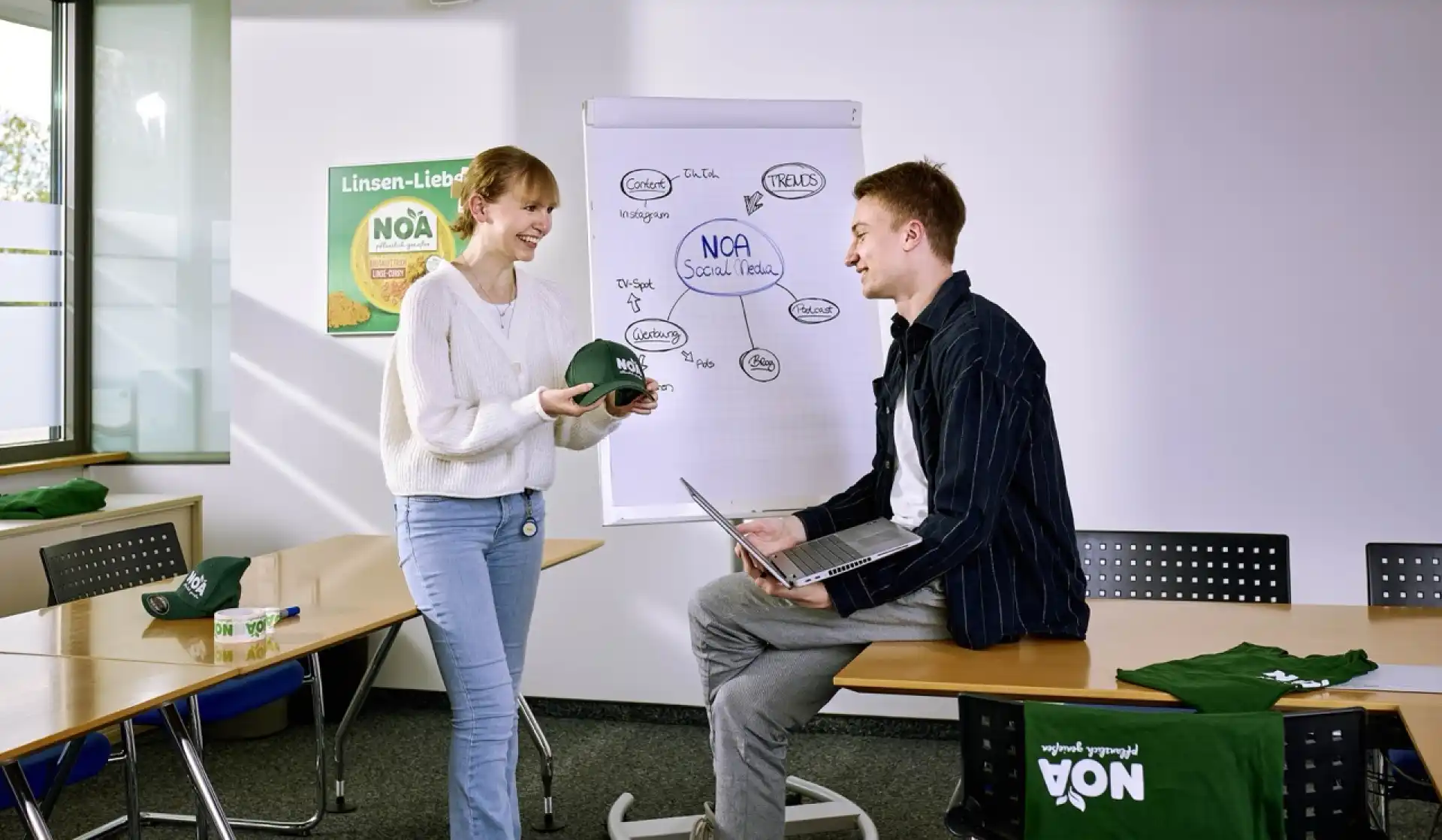 Zwei Auszubildende der Verwaltung besprechen neue Werbemittel im Sitzungszimmer.