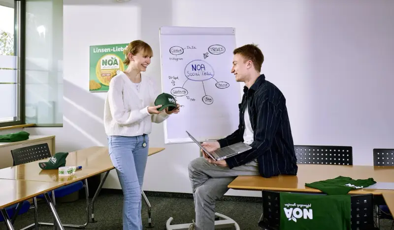 Zwei Auszubildende der Verwaltung besprechen neue Werbemittel im Sitzungszimmer.