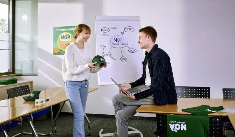 Zwei Auszubildende der Verwaltung besprechen neue Werbemittel im Sitzungszimmer.
