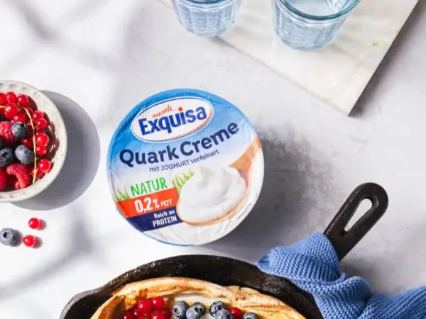 Exquisa QuarkCreme Natur steht neben einer schwarzen Metallpfanne, die ein Dutch Baby Pfannkuchen mit QuarkCreme Natur und Früchten enthält.