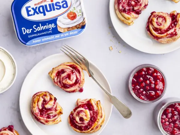 Exquisa Frischkäse Der Sahnige Natur steht auf einem hellen Holztisch umringt von gebackenen Cranberry-Rosen.