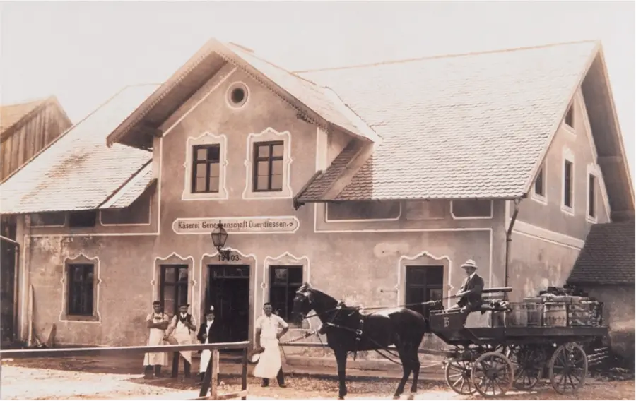 Historische Aufnahme eines Wohn- und Betriebsgebäudes mit Pferdegespann vor dem Haus.