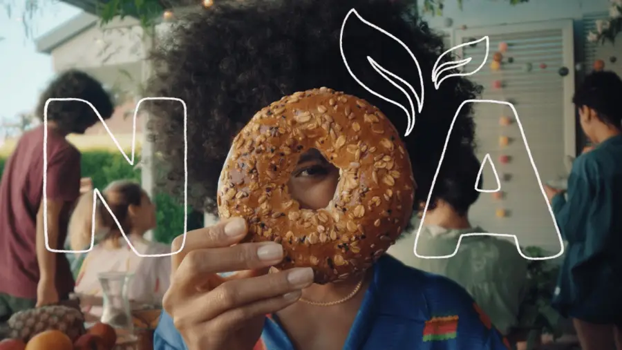 Ausschnitt aus dem NOA-TV-Spot: Person hält Donut vor das Gesicht mit NOA im Hintergrund.