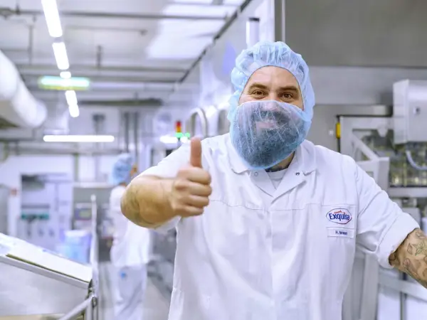 Ein Produktionsmitarbeiter in Hygienekleidung lächelt in die Kamera und gibt einen Daumen hoch.