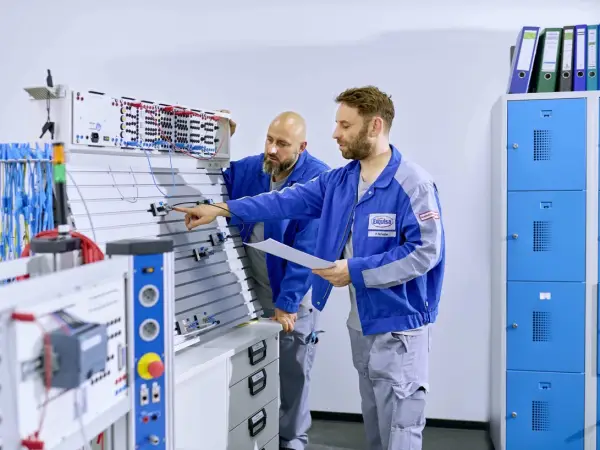 Zwei Mitarbeitende der Technik stehen an einem Elektropult und arbeiten.