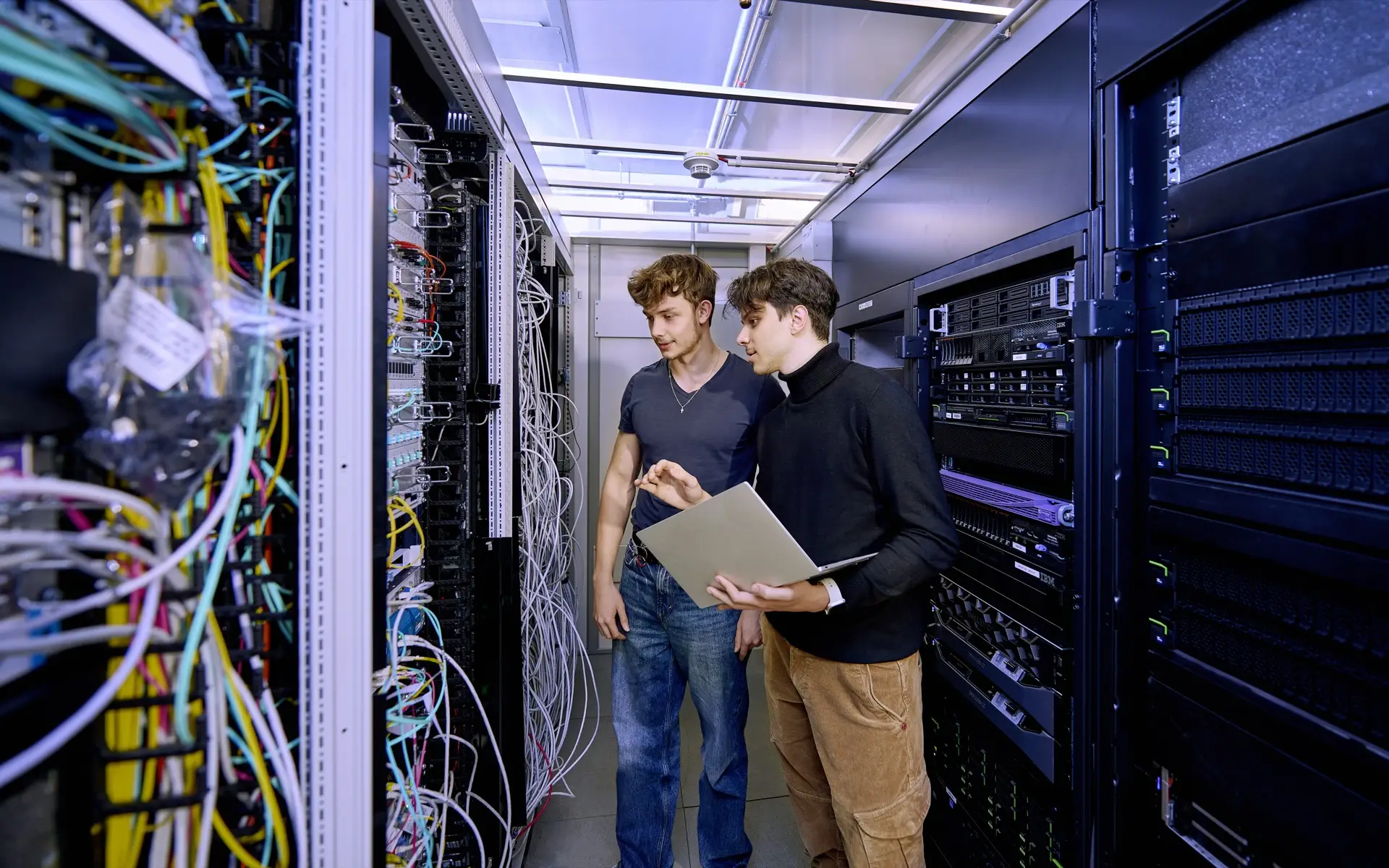 Ein IT-Mitarbeiter erklärt seinem Auszubildenden etwas im Serverraum.