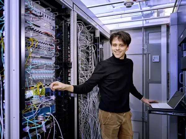 Ein Mitarbeiter der IT steht im Serverraum und lächelt in die Kamera.