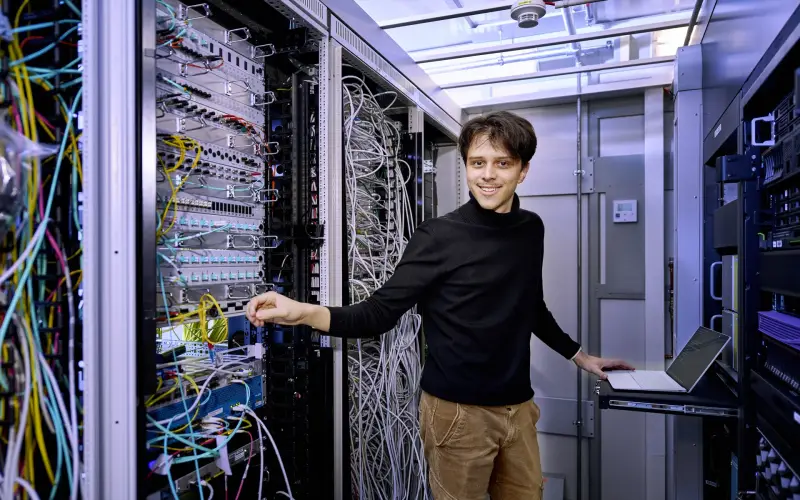 Ein Mitarbeiter der IT steht im Serverraum und lächelt in die Kamera.