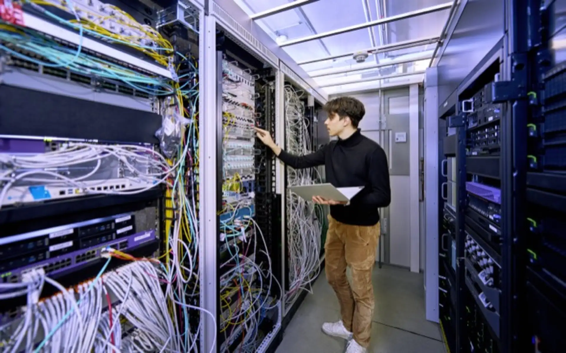 Ein IT-Mitarbeiter steht in einem Serverraum und kontrolliert die Geräte.