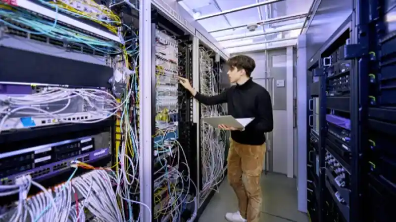 Ein IT-Mitarbeiter steht in einem Serverraum und kontrolliert die Geräte.