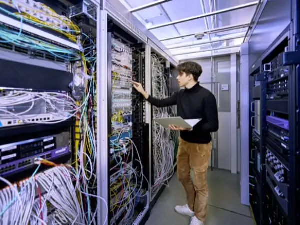 Ein IT-Mitarbeiter steht in einem Serverraum und kontrolliert die Geräte.