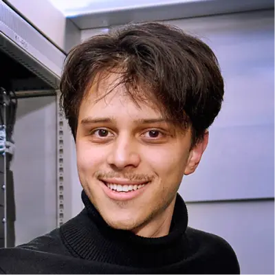 Ein Mitarbeiter der IT steht im Serverraum und lächelt in die Kamera.