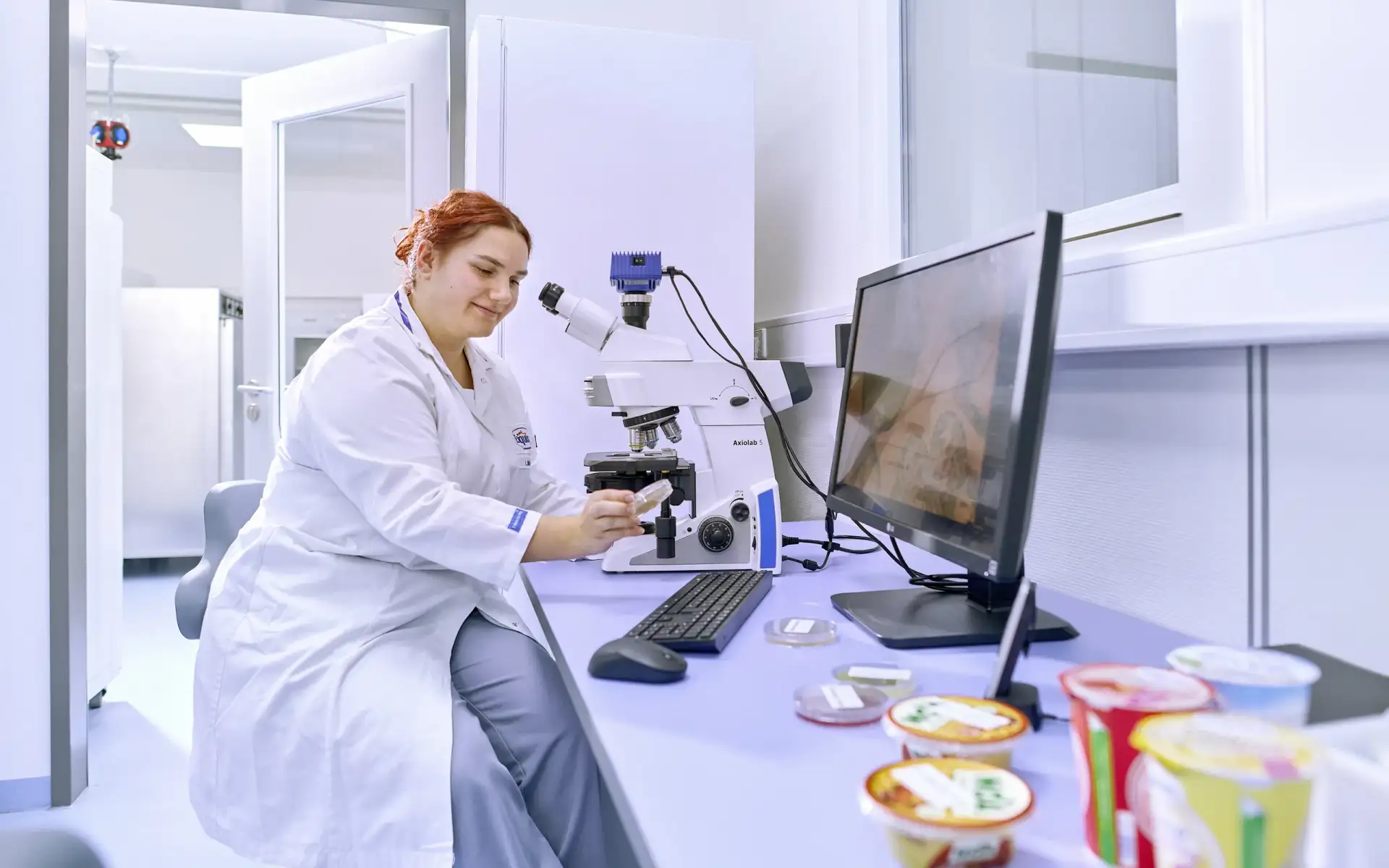 Labor Mitarbeitende sitzt an einem Mikroskop und kontrolliert Produktqualität.