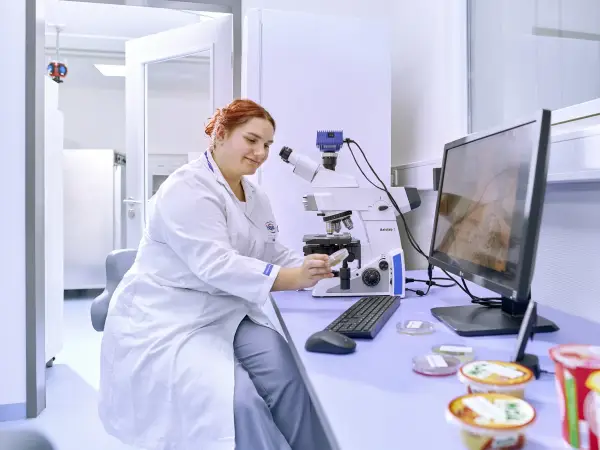 Labor Mitarbeitende sitzt an einem Mikroskop und kontrolliert Produktqualität.