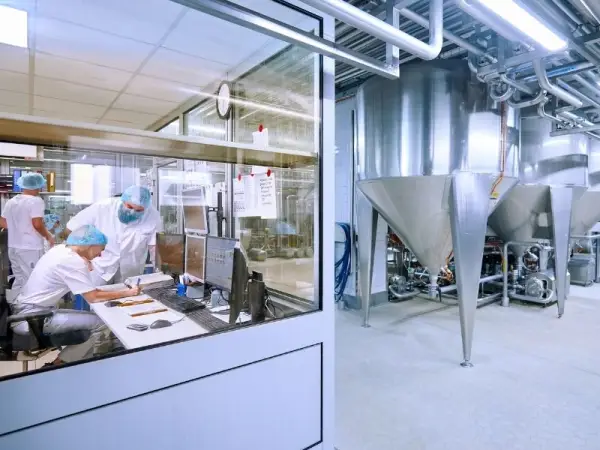 Zwei Produktionsmitarbeiter dokumentieren Daten im Kontrollraum vor großen Edelstahltanks in der Produktionshalle.
