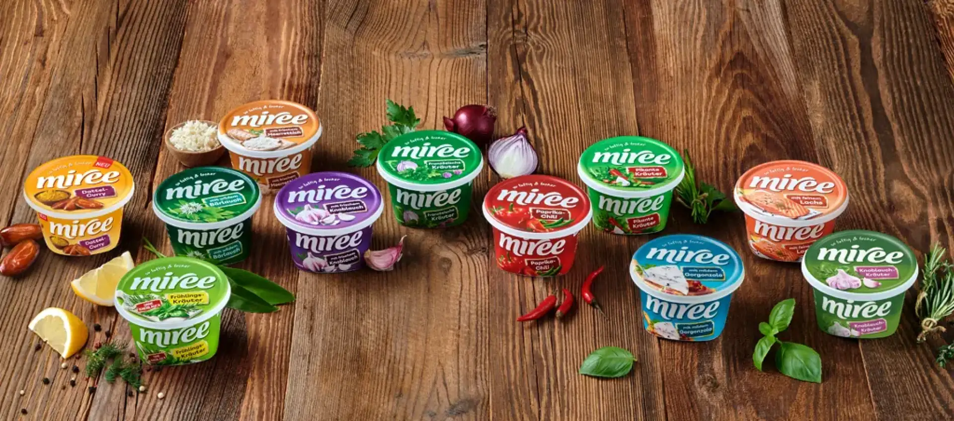 Alle erhältlichen miree Produkte stehen auf einem braunen Holztisch umbringt von ihren geschmacksgebenden Zutaten.