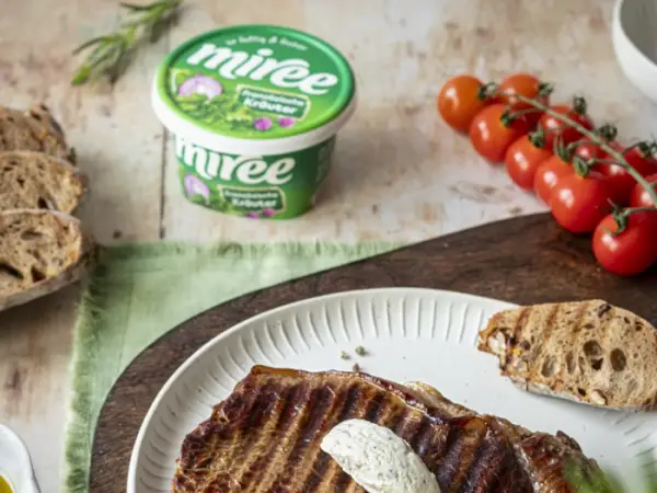 Ein miree Becher steht mit einem Essteller auf einem Tisch. Auf dem Teller befindet sich ein gegrilltes Rindersteak mit miree Nocke darauf.
