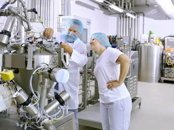 Eine Auszubildende der Produktion steht mit ihrem Ausbilder an einer Produktionsmaschine und lernt deren Bedienung.