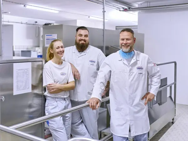 Zwei Produktionsmitarbeitende stehen an einer Produktionsmaschine. Einer bedient die Maschine und einer füllt Becher nach.
