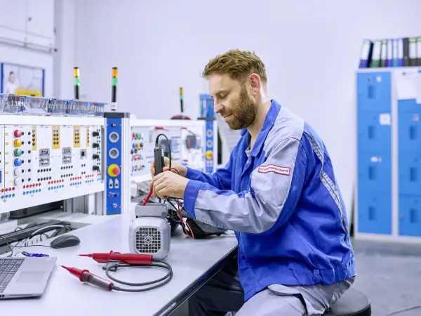 Technik Mitarbeitender sitzt an einem Elektropult und arbeitet.